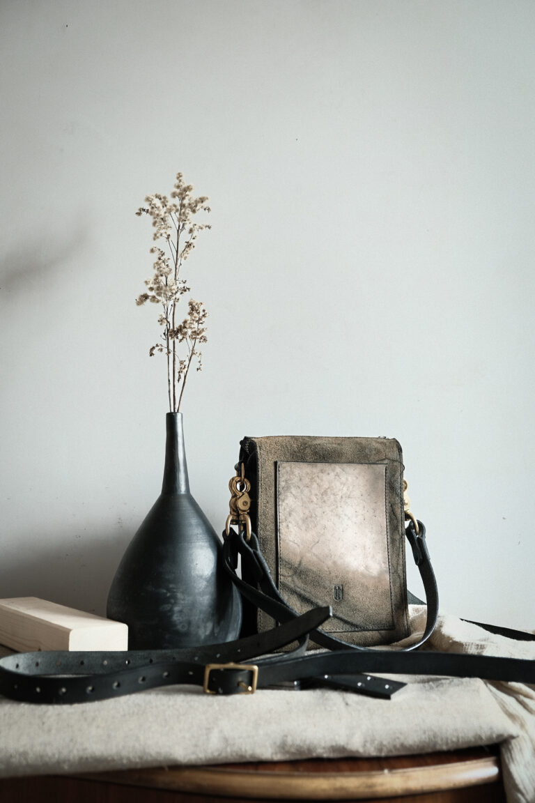 Die crossbody geometrica Tasche zur Ansicht neben einer Vase und auf einem Tuch liegend