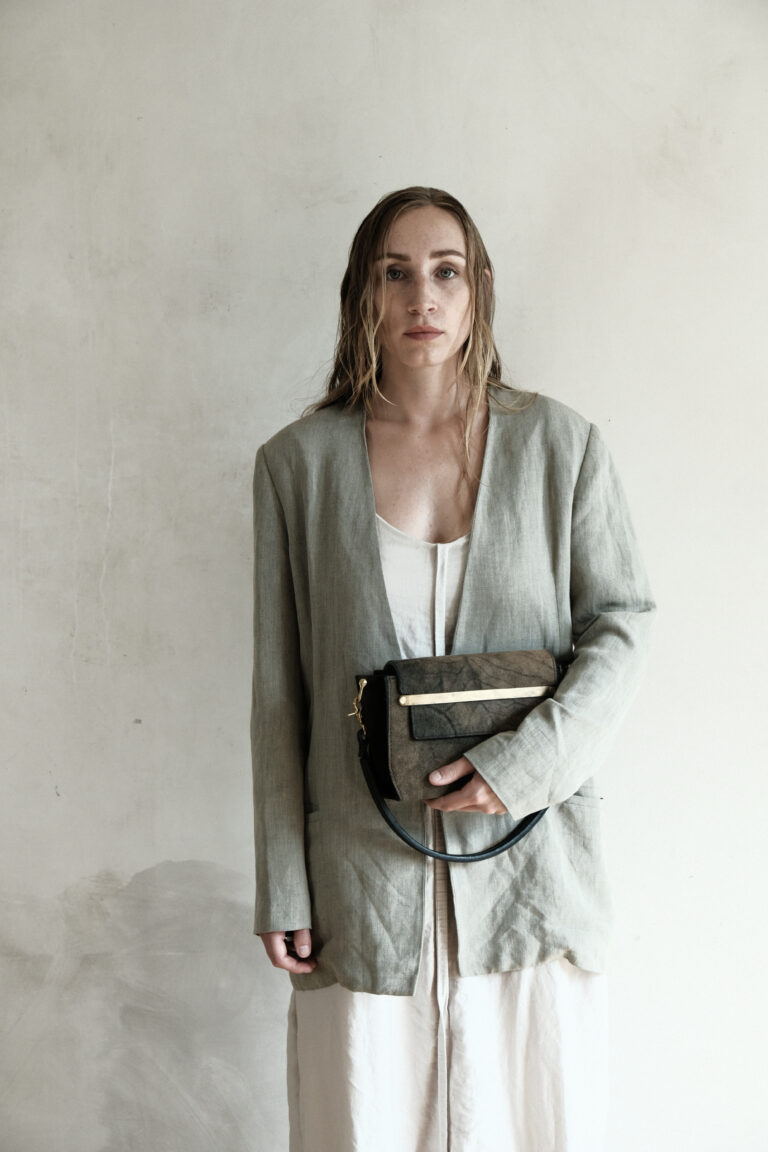 Model holds the subtilis small bag in her arms. The brass fittings on the bag are particularly striking